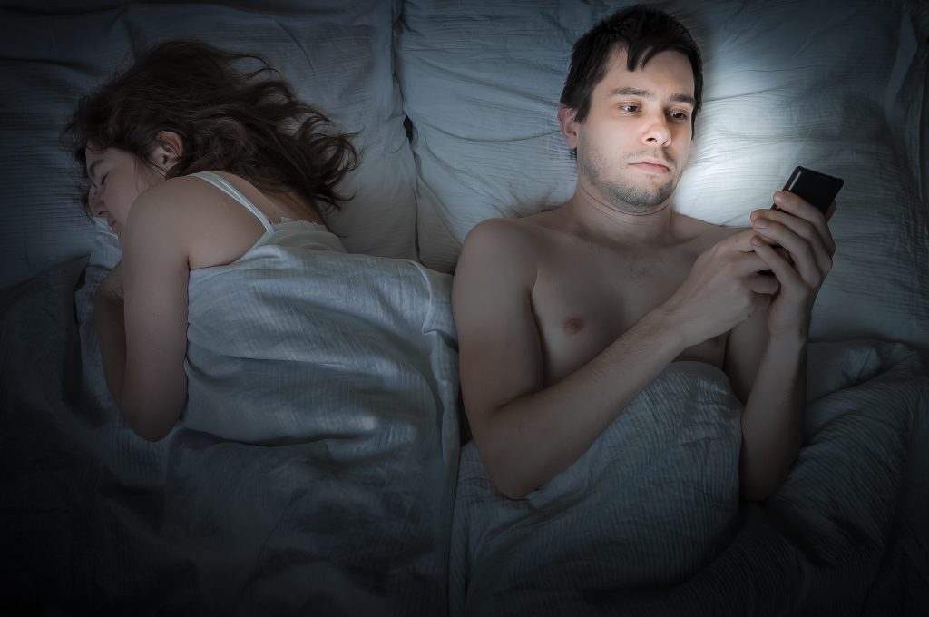 man texting while girlfriend sleeps