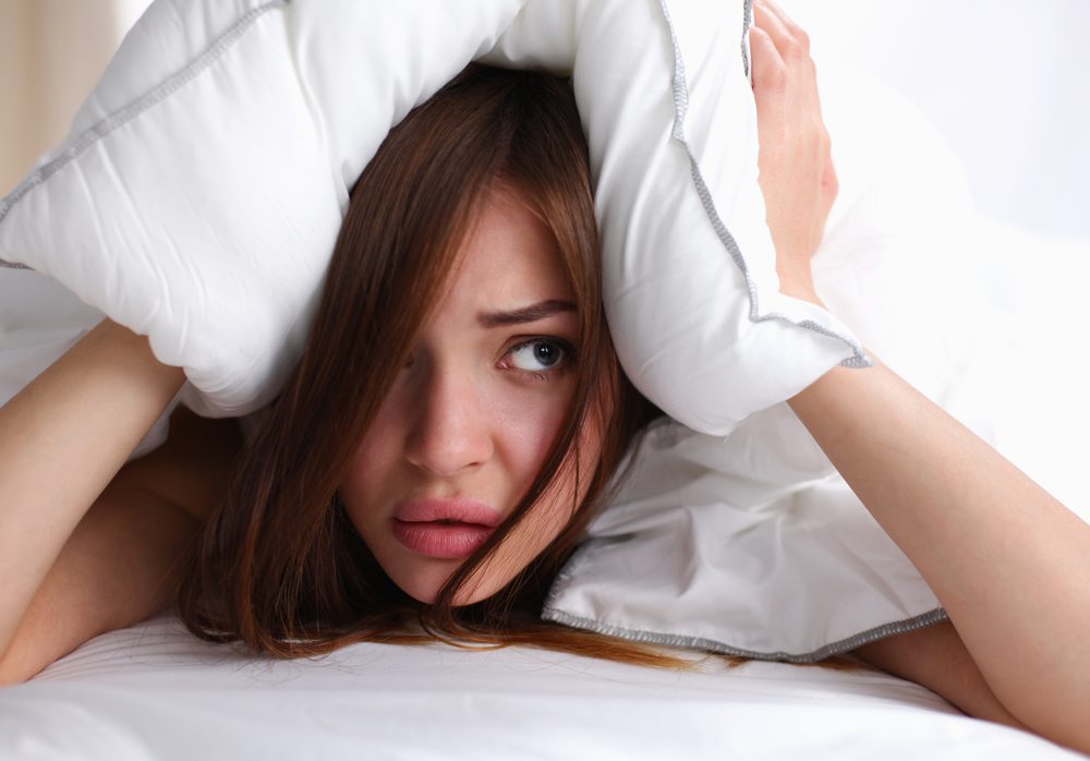 woman hiding under pillow