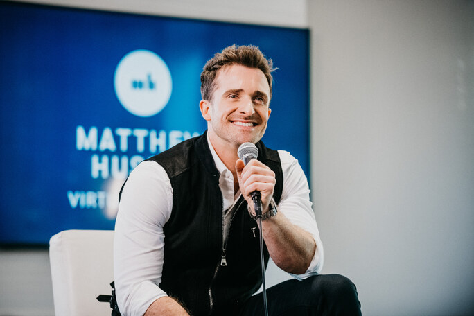 A photo of Matthew Hussey smiling and holding a microphone